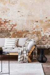 Pillows and blanket on wooden couch against red brick wall in flat interior with table. Real photo