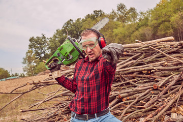Lumberjack with chainsaw and pile of cut woods.