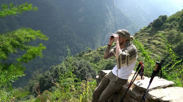 Hiker looking through binoculars on a trekking trail to the Annapurna base camp, the Himalayas, Nepal.