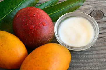 Mango body butter in a glass bowl and fresh ripe organic mango fruits on old wooden background.Spa,natural oils,organic cosmetic or skin care ecological concept.