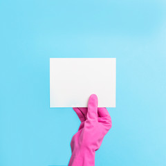 female hand in pink gloves holds an empty card on a blue background. cleaning service concept. Flat lay, Top view