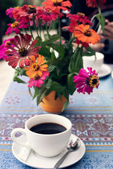 A cup of black coffee and flowers vase on table.