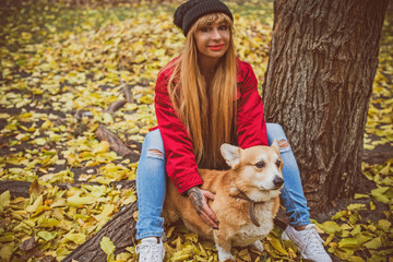 Naklejka na ściany i meble Woman with Red dog of Corgi breed for a walk in the city streets. The life of dogs in cities. Dog lover with her pet 
