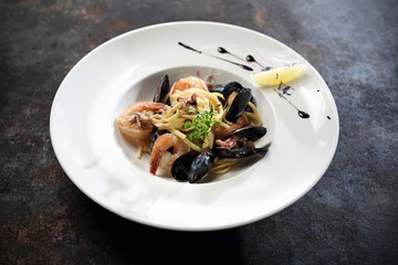 Spaghetti frutti di mare  krewetki, małże, ośmiorniczki, ślimaki, paluszki krabowe. Apetyczna, wykwintna potrawa pięknie podana na białym talerzu. © foodandcook