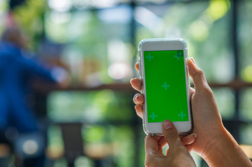 The view is cut out of the woman's hand holding a smart phone with a blank screen for text message space or text message content reading on a mobile phone. Green screen