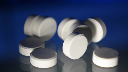 A bunch of white round pills on the table. On a blue background. Close up.