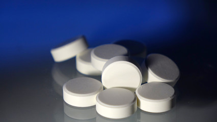 A bunch of white round pills on the table. On a blue background. Close up.