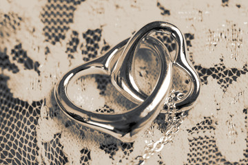 Silver linked heart necklace with chain on a lace fabric background with toning