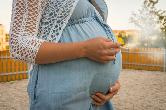 Pregnant woman smoking cigarette on the park