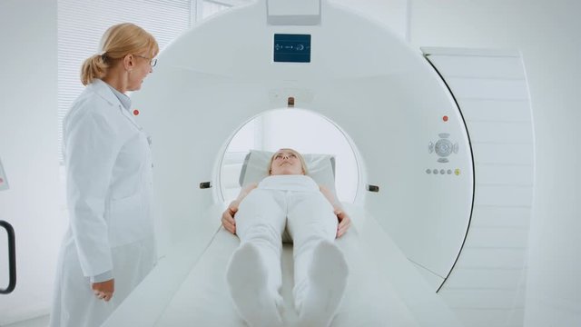 In Medical Laboratory Female Radiologist Controls MRI or CT Scan with Female Patient Undergoing Procedure. High-Tech Modern Medical Equipment. 