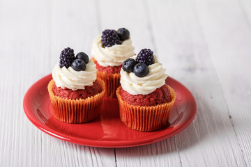 Tasty red velvet cupcakes with blueberry and blackberry on wooden table.