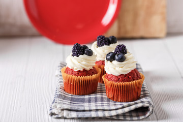 Tasty red velvet cupcakes with blueberry and blackberry on wooden table.