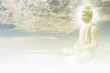 The white Greek sitting Buddha image covered by moss in the sky background and white cloud on the sky and there is aura at the Buddha head. 