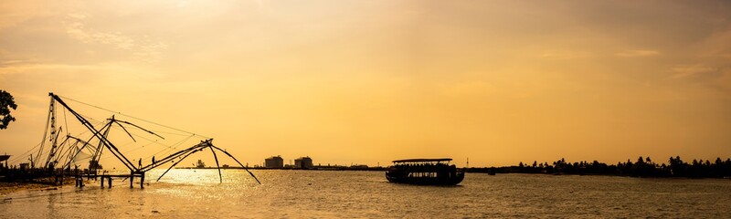 Fototapeta premium Panoramic silhouette of chinese fishnets on sunset at Fort Kochi, Kerala, India.