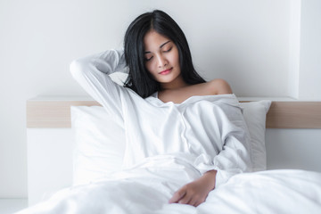 Beautiful young pretty Asian woman wake up and make happy smile with white shirt at the white bed in the morning. 