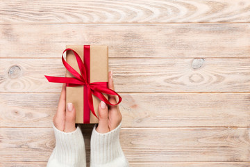 Woman hands give wrapped valentine or other holiday handmade present in paper with red ribbon....