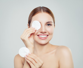 Cheerful woman removing face makeup with a cotton pad