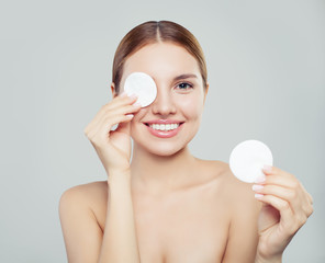 Cheerful young woman removing face makeup with a cotton pad