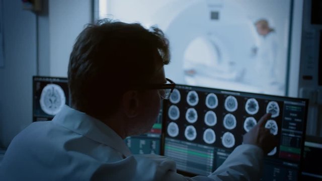 In Medical Laboratory Patient Undergoes MRI or CT Scan Process under Supervision of Radiologist, in Control Room Doctor Watches Procedure and Monitors with Brain Scans Results.