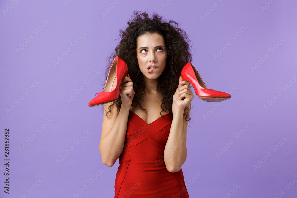 Sticker Image of caucasian woman 20s wearing red dress holding high heels shoes, standing isolated over violet background