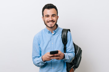 Portrait of smiling young man in casual holding smartphone and looking at the camera standing over...