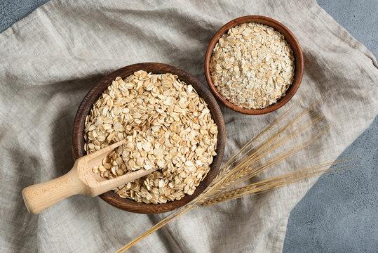 Rolled oats, oat flakes in wooden bowl and golden wheat ear on linen textile. Table top view. Healthy lifestyle, dieting, healthy eating concept