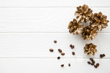 Golden pine cones with coffee beans on white wooden table background, top view, copy space.