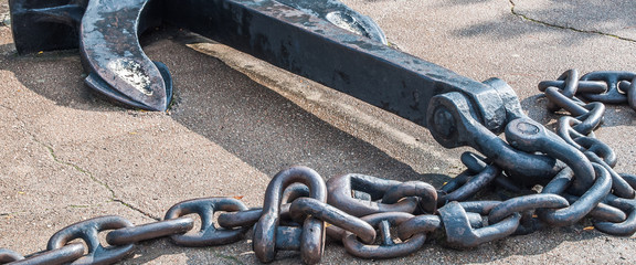 Heavy iron metal ship anchor with chain on gray asphalt.