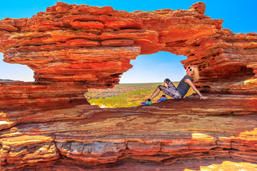 Blonde happy woman sitting inside the iconic rock arch in red sandstone of Nature's Window,...