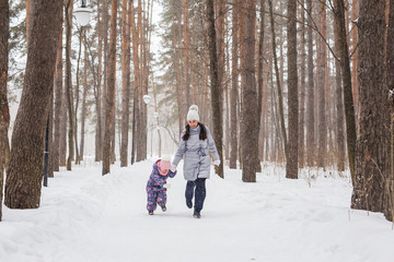 Fototapeta na wymiar Winter, childhood and people concept - mother is walking with her little daughter in snowy forest