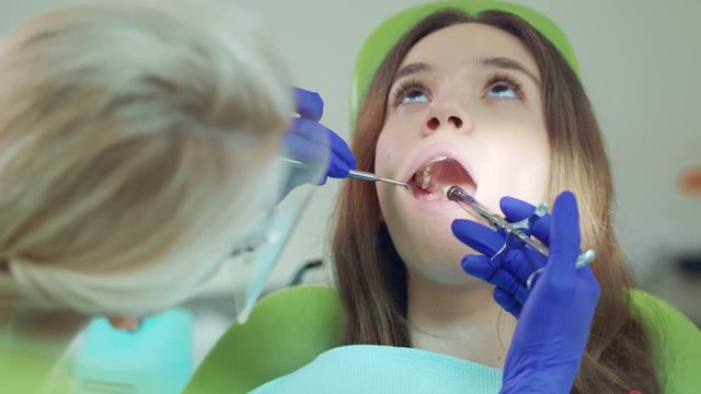 Dentist doing anesthetic injection in patient tooth. Woman doctor using medicine syringe. Close up of female patient in dentist chair. Professional dental anesthesia