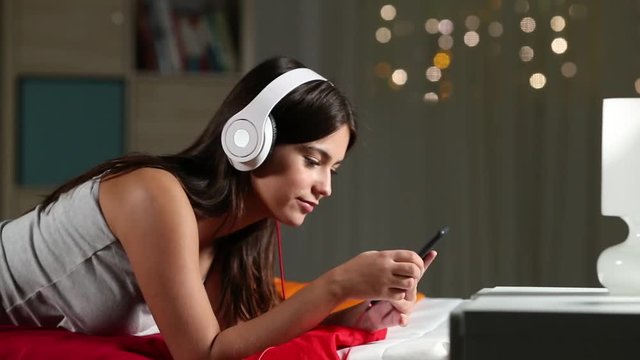 Profile of a happy teen listening to music relaxing on a bed in the night at home