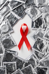 top view of aids awareness red ribbon and silver condoms on white background
