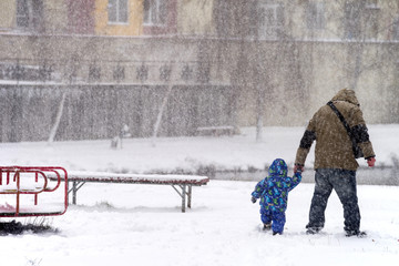 Man with child make their way through the blizzard in the city. Selective focus.