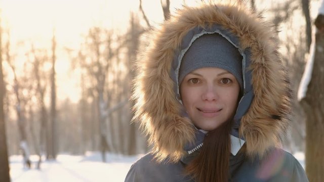 Close-up woman face in fur hood looking in camera and smiling in winter sunny park. Right on video