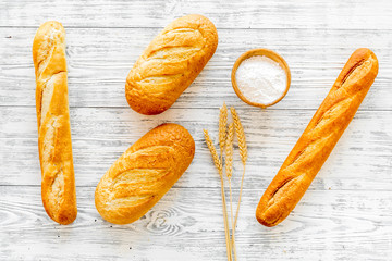 White bread. Fresh rustic homemade bread and loaf on tablecloth decorated with ears and flour on white wooden background top view