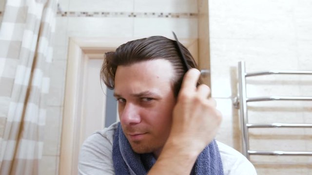 Young shaggy man combs hair with a comb arter head washing.