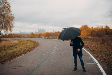 Young man in black coat walking in the rain with umbrella