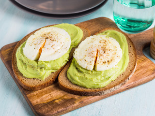 Rye bread avocado toasts with poached egg on wooden serving board. Brunch lunch meal