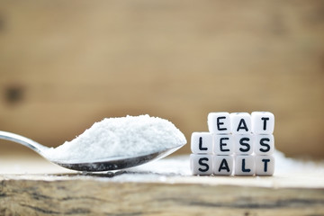 Eat less salt recommendation with plastic letters  and granulated salt on wooden chopping board 