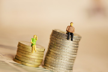Income inequality by gender with human miniature silhouettes on pile of coins