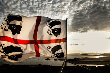 Bandiera della Sardegna con i quattro mori e sullo sfondo la costa di Capo spargimento/Teulada al tramonto - obrazy, fototapety, plakaty