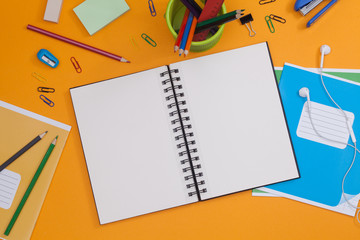Empty spiral notebook with white page and multicolored stationery on a orange table. Workplace with...