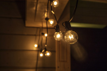 Decorative street lights hanging on the terrace of a wooden house at night. Old decorative lamps, festive lighting - Powered by Adobe