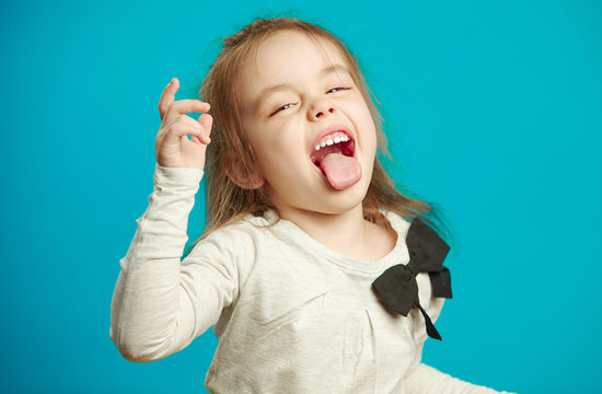 Cute little girl in white T-shirt makes funny face and shows tongue