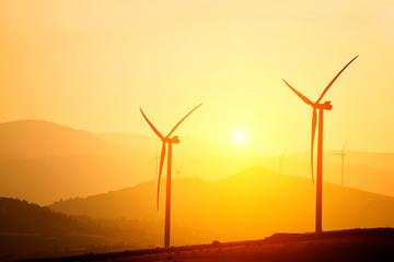 Obraz premium Wind power generators on the background of silhouettes of mountain peaks. Simplicity and minimal lines. Beautiful landscape of the power of nature. 