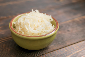 Sauerkraut in a plate on a wooden background.