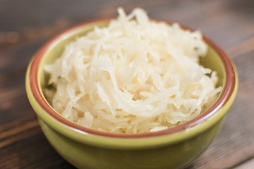 Sauerkraut in a plate on a wooden background.
