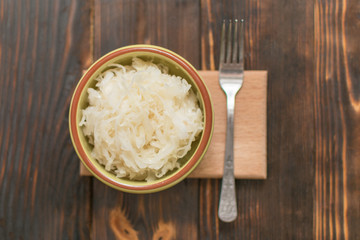 Sauerkraut in a plate on a wooden background.