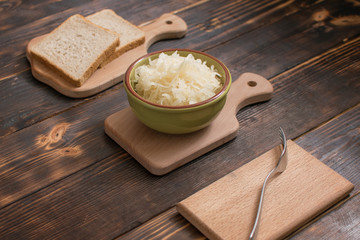 Sauerkraut in a plate and a piece of bread on a wooden background.